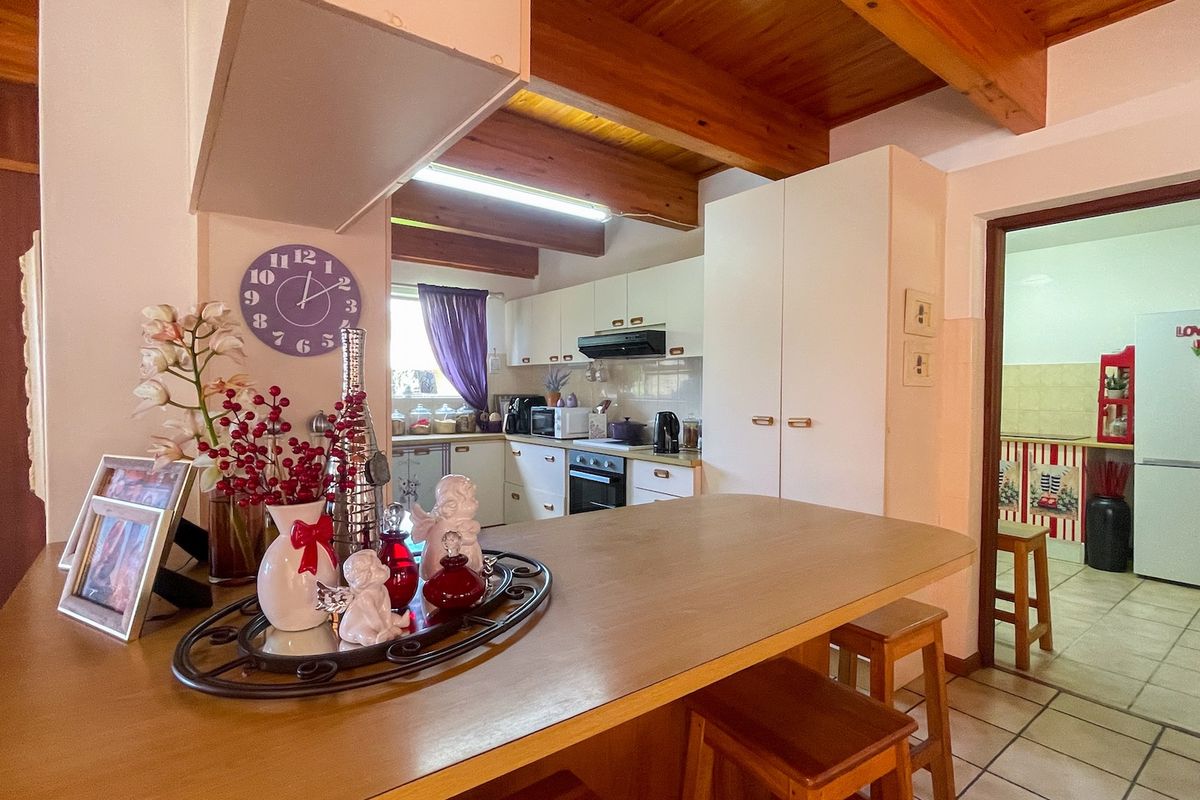 A functional kitchen featuring exposed timber ceiling beams, built-in cabinetry, and a breakfast counter, with an adjacent scullery area visible through the doorway.