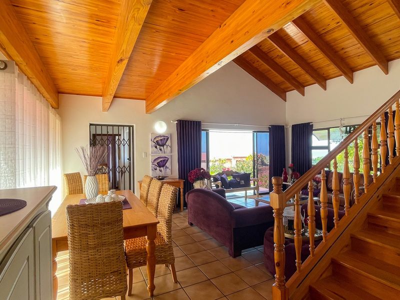 Spacious open-plan living and dining area featuring a vaulted timber ceiling, exposed beams, and a wooden staircase, with direct access to the outdoor patio.