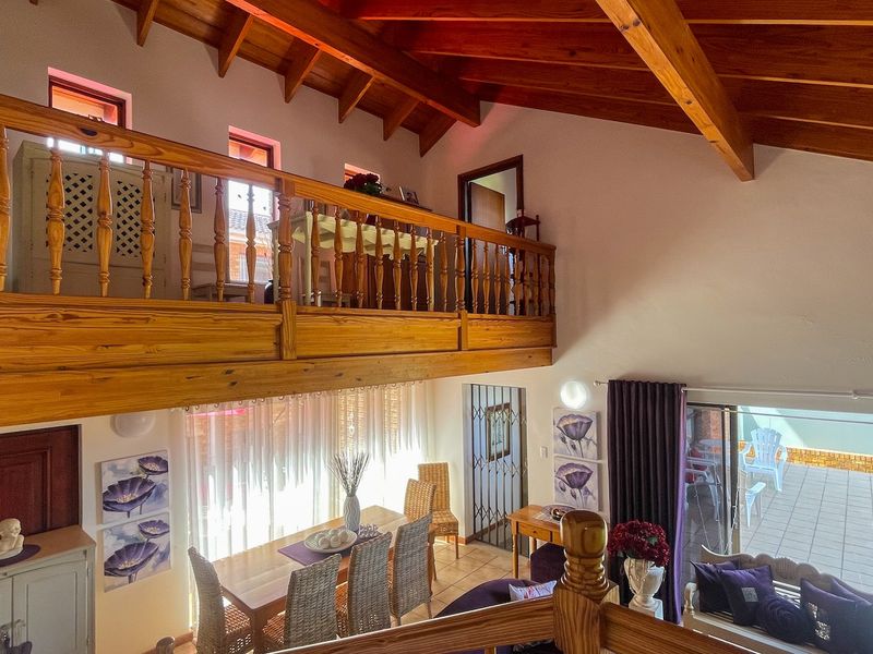 Spacious open-plan living area featuring high vaulted timber ceilings, a mezzanine level with wooden balustrade, and direct access to an outdoor tiled patio.