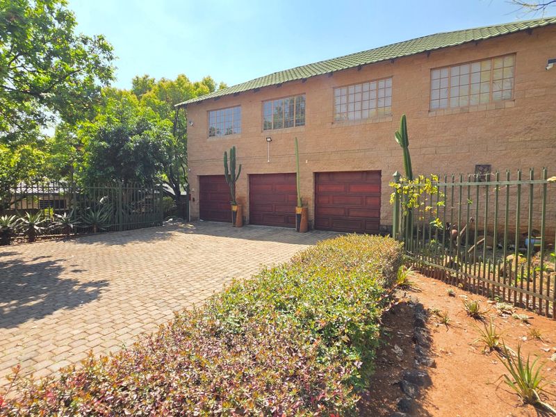Front exterior view of a property featuring a triple garage, paved driveway, and secure metal fencing with established garden surroundings.