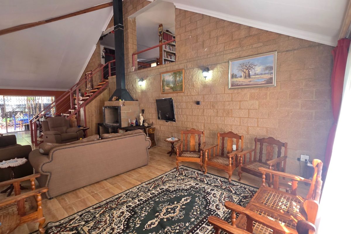 Spacious living room featuring a vaulted ceiling, exposed brick wall, built-in fireplace, and a staircase leading to a mezzanine level.
