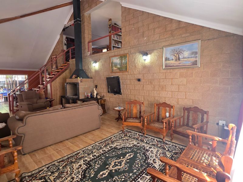 Spacious living room featuring a vaulted ceiling, exposed brick wall, built-in fireplace, and a staircase leading to a mezzanine level.