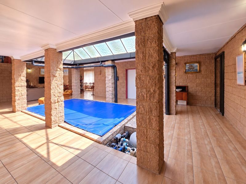 An indoor swimming pool area featuring a large skylight, stone-clad support pillars, and tiled flooring, providing a unique and sheltered recreational space.