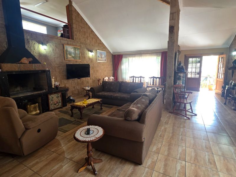 Spacious living room featuring exposed brick walls, a vaulted ceiling, and a built-in fireplace, with tiled flooring throughout and direct access to the outdoors.