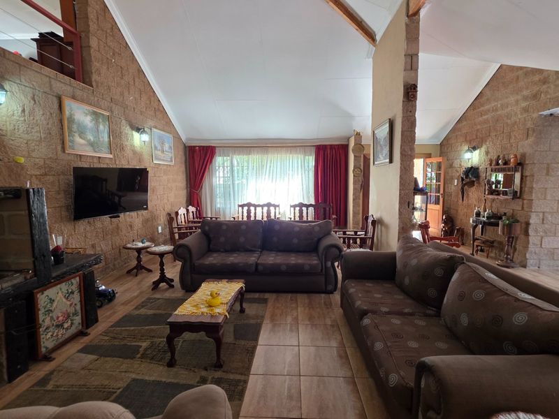 Spacious open-plan living area featuring high vaulted ceilings with exposed timber beams, rustic brick walls, and a built-in fireplace.