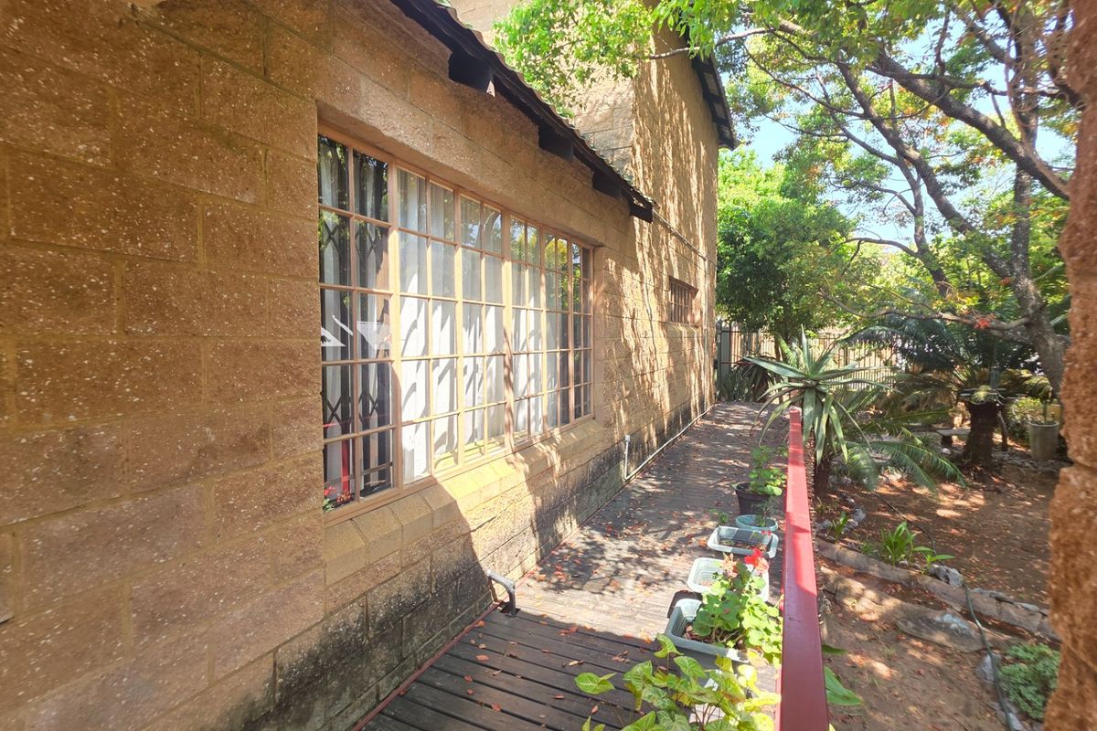 A rear exterior view of the property featuring stone masonry walls, large metal-framed windows, and a wooden deck with a metal railing.