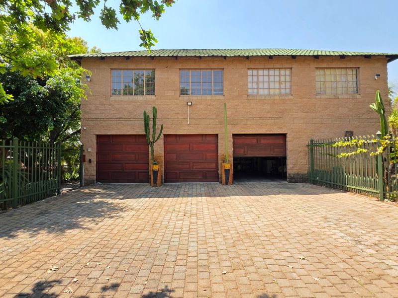 Front view of a double-story house featuring a triple garage with wooden doors, a paved driveway, and secure metal perimeter fencing.