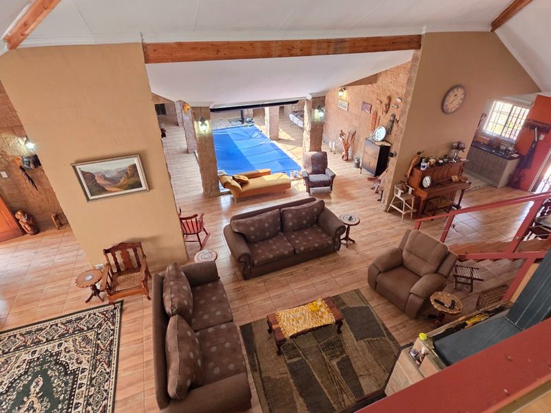 Spacious open-plan living area featuring vaulted ceilings with exposed timber beams, tiled flooring, a stone feature wall, and an integrated indoor swimming pool.