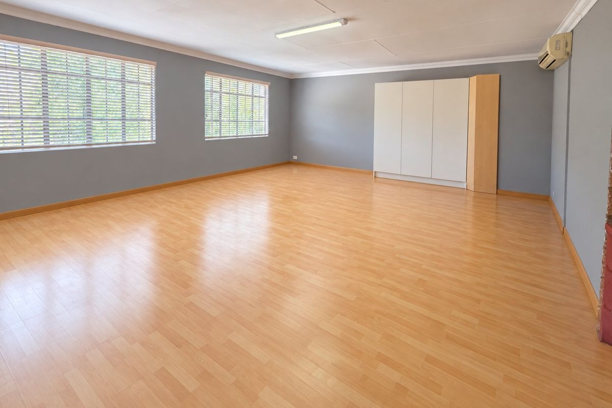 Spacious, empty bedroom featuring light laminate flooring, grey walls, built-in storage cupboards, and an installed air conditioning unit.