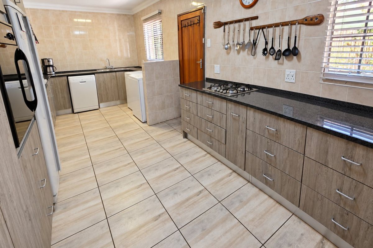 A functional kitchen featuring wood-look cabinetry, granite countertops, a gas hob, built-in oven, and neutral tiled flooring throughout.