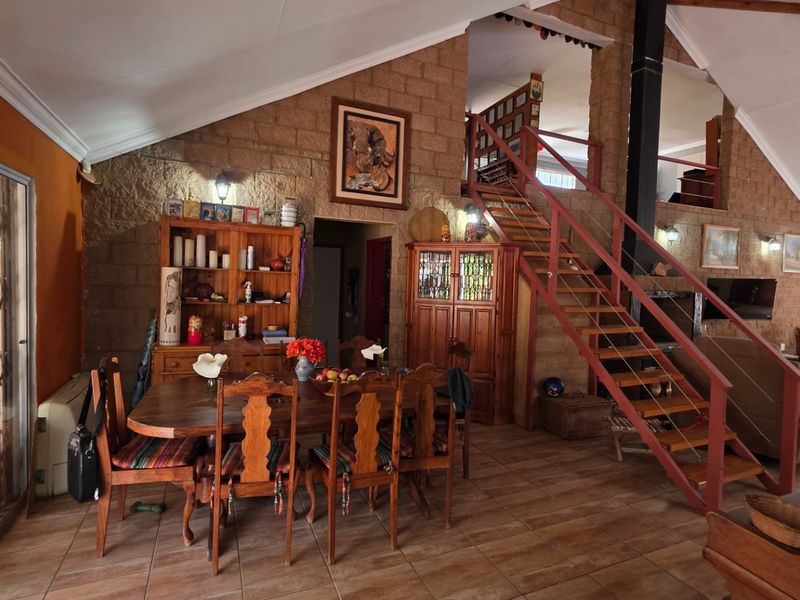Spacious open-plan living and dining area featuring exposed brick walls, vaulted ceilings, tiled floors, and a central staircase leading to an upper level.