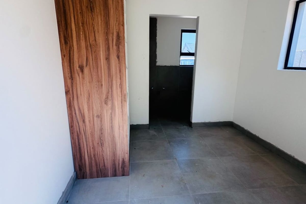 An empty bedroom featuring modern wood-finish built-in cupboards, large format floor tiles, and neutral walls, ready for final finishing touches.