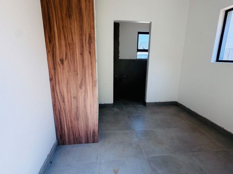 An empty bedroom featuring modern wood-finish built-in cupboards, large format floor tiles, and neutral walls, ready for final finishing touches.