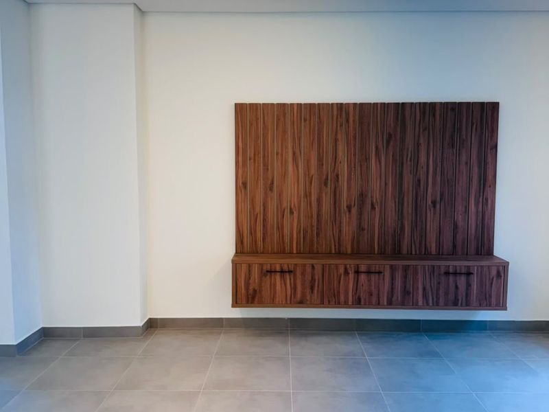 A modern, minimalist living area featuring large format floor tiles, a sleek built-in wooden media console, and recessed ceiling lighting.