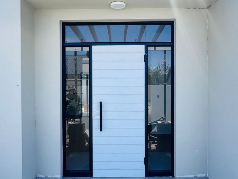 A modern front entrance featuring a white horizontal-panel door with black hardware, flanked by glass sidelights under a white timber pergola.