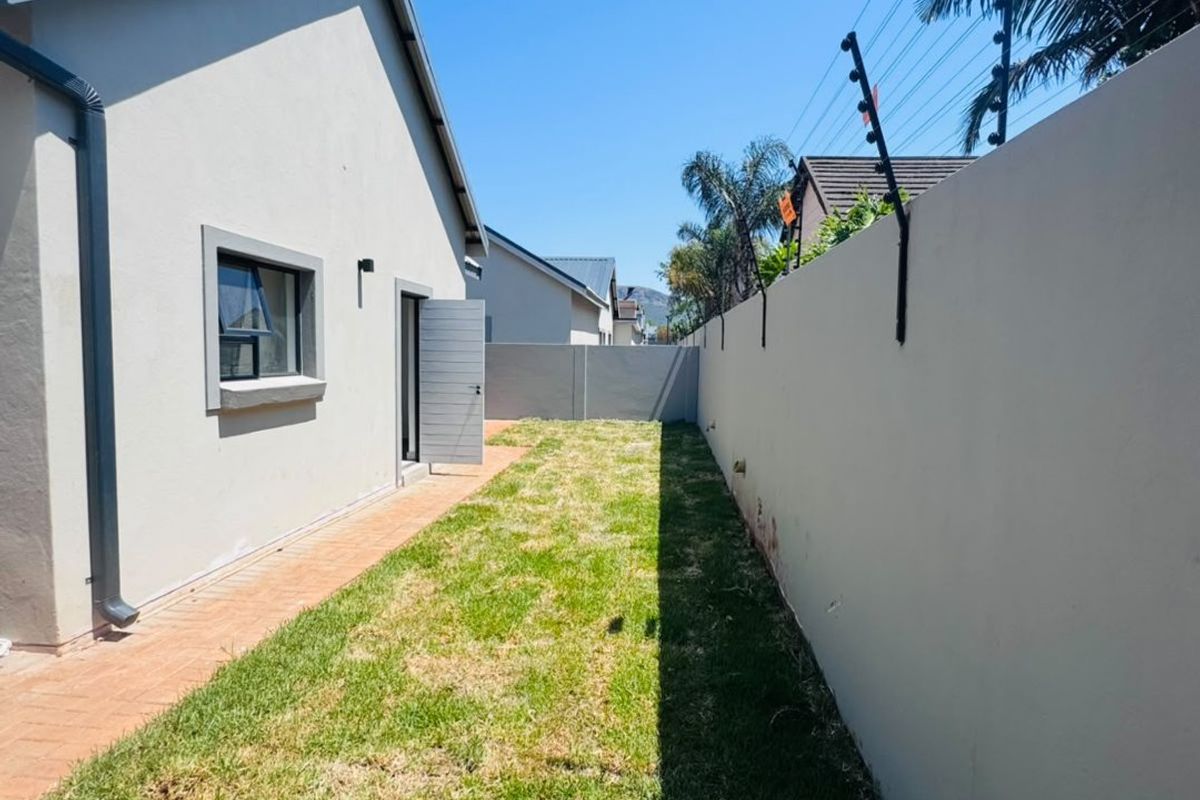 A side garden area featuring a paved walkway, a well-maintained lawn, and a high boundary wall equipped with electric fencing for added security.