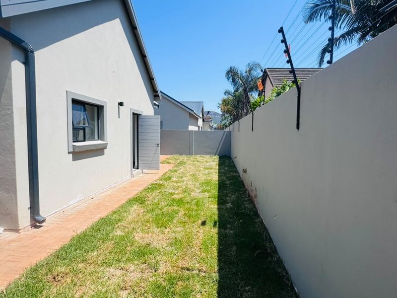 A side garden area featuring a paved walkway, a well-maintained lawn, and a high boundary wall equipped with electric fencing for added security.