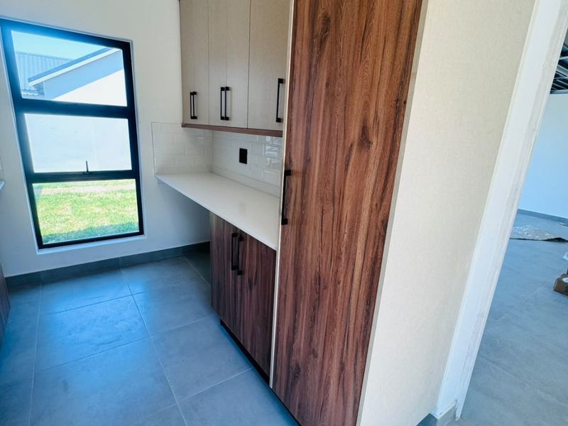 A modern, clean scullery area featuring contemporary wood-grain and neutral cabinetry, stone countertops, subway tile backsplash, and large format floor tiles.