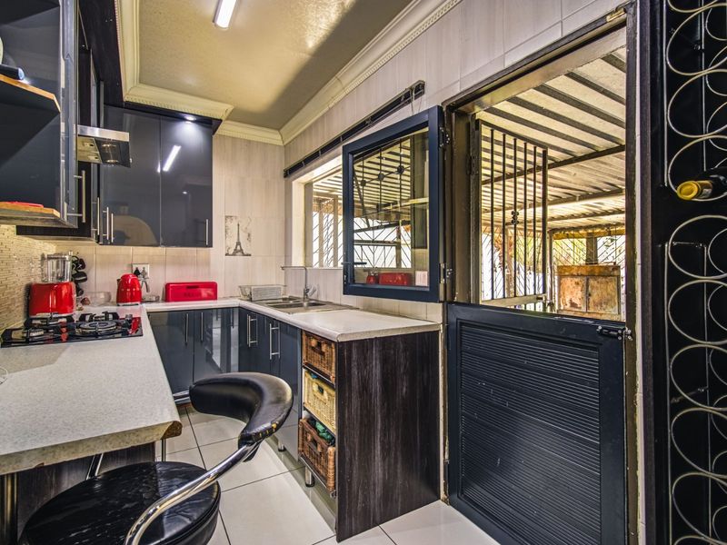 Compact kitchen featuring dark cabinetry, gas hob, extractor fan, and direct access to an outdoor area through a security door.