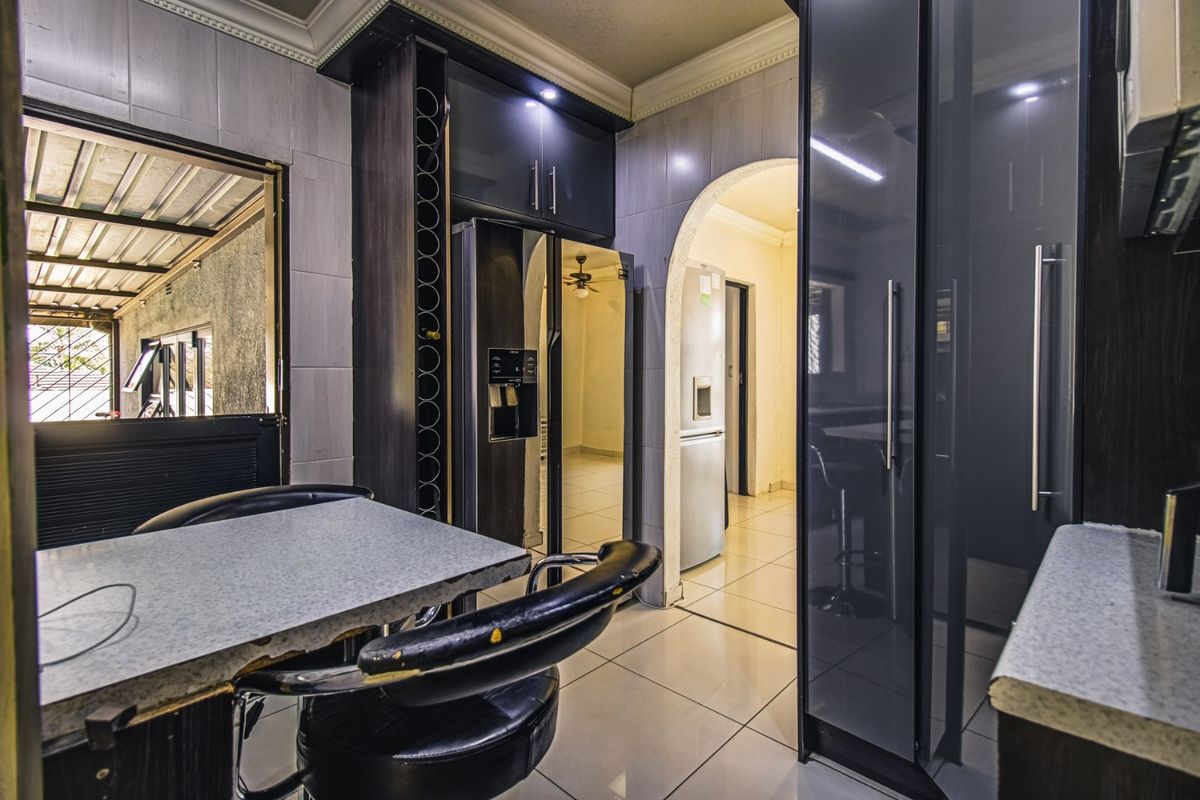 A modern kitchen featuring dark cabinetry, tiled flooring, and an arched entryway leading to adjacent living spaces.