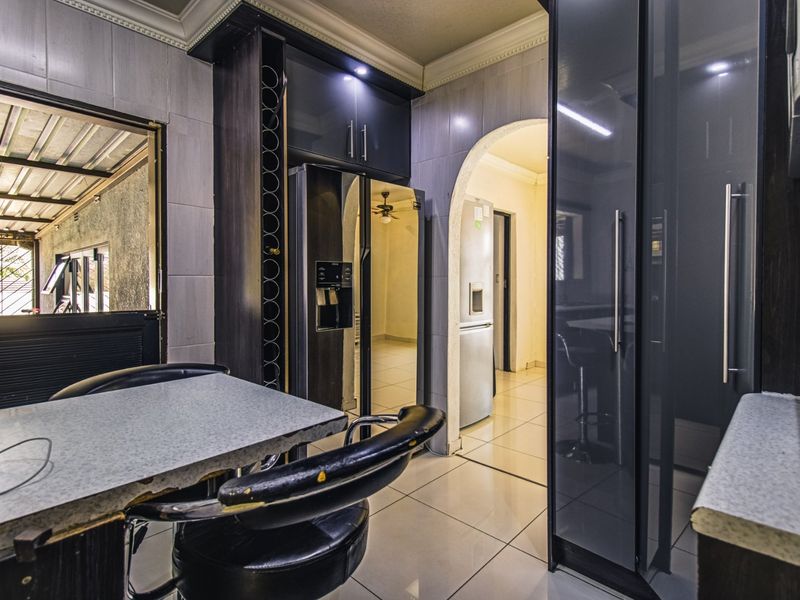 A modern kitchen featuring dark cabinetry, tiled flooring, and an arched entryway leading to adjacent living spaces.