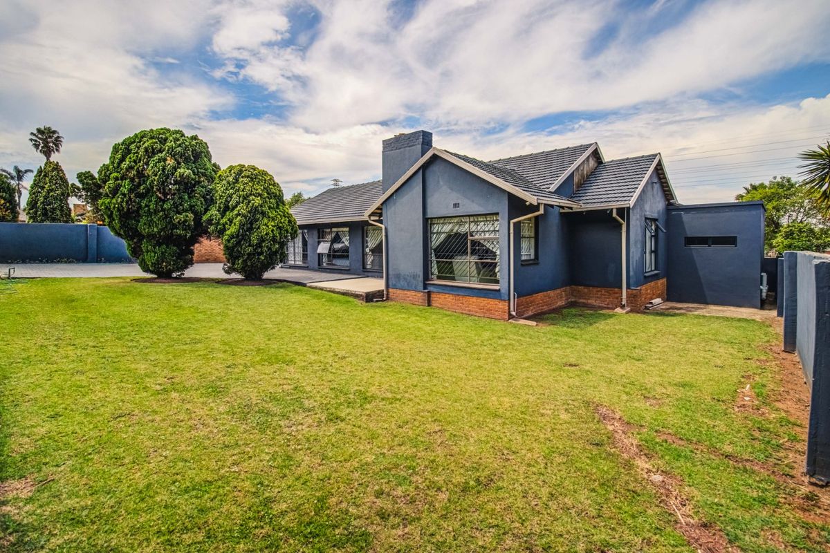 Rear view of a detached house featuring a dark blue painted facade, tiled roof, brick chimney, and a spacious lawn with a paved patio area.
