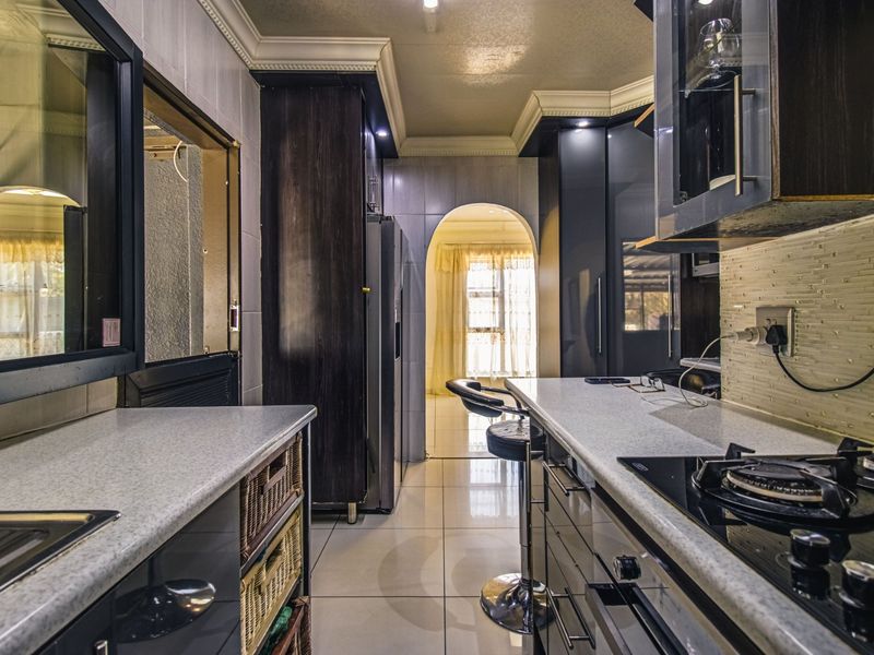 Modern kitchen featuring dark cabinetry, stone countertops, integrated gas hob, and tiled flooring, leading through an archway to an adjacent living area.
