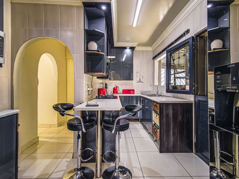 Modern kitchen featuring dark cabinetry, stone countertops, built-in appliances, and a breakfast bar, complemented by tiled flooring and a distinctive architectural archway.