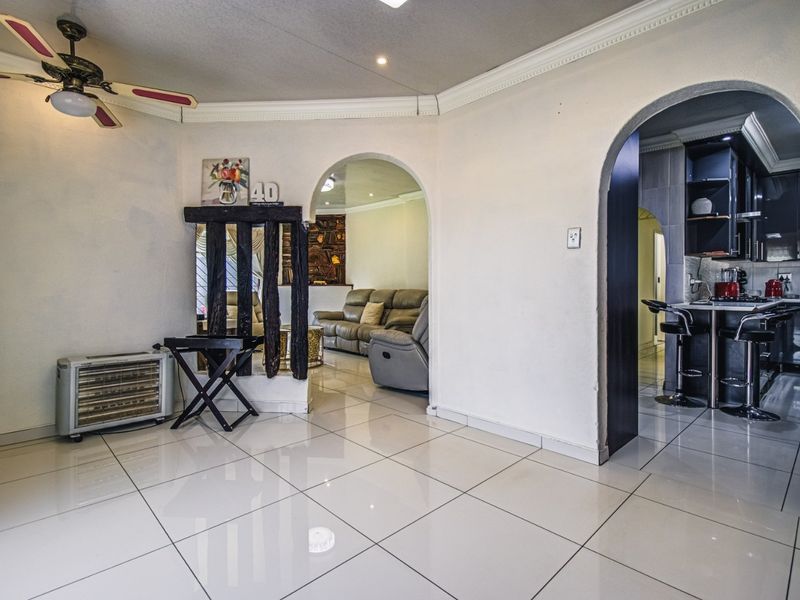 Open plan living area featuring tiled floors, decorative archways, and crown molding, with a clear transition into the adjacent kitchen and lounge spaces.