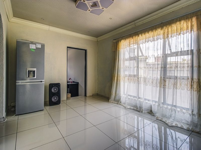 A spacious, empty living area featuring large windows, tiled flooring, and decorative ceiling cornicing, offering a blank canvas for interior design.
