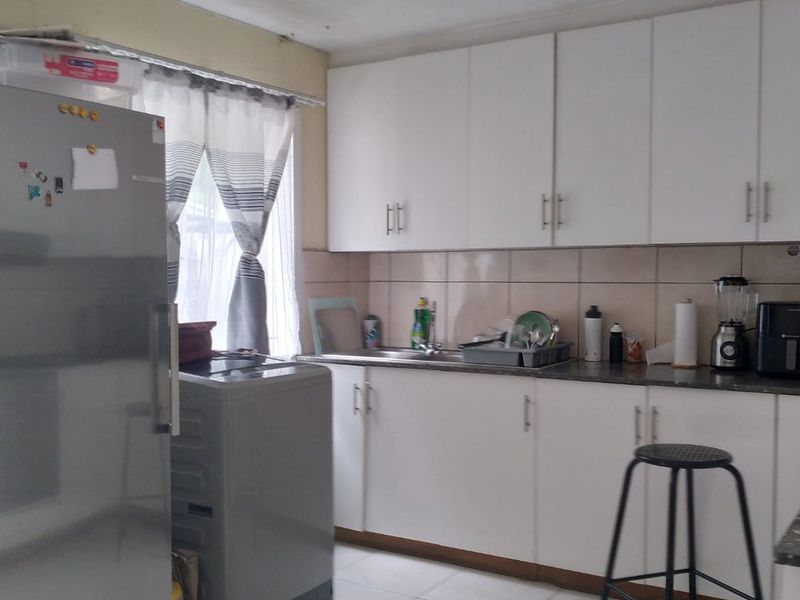 A functional kitchen featuring white cabinetry, tiled backsplash, and tiled flooring, providing a practical workspace with integrated sink and storage.