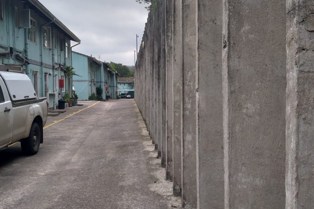 A view of the rear exterior area featuring a long concrete boundary wall and a paved driveway alongside the apartment building facade.