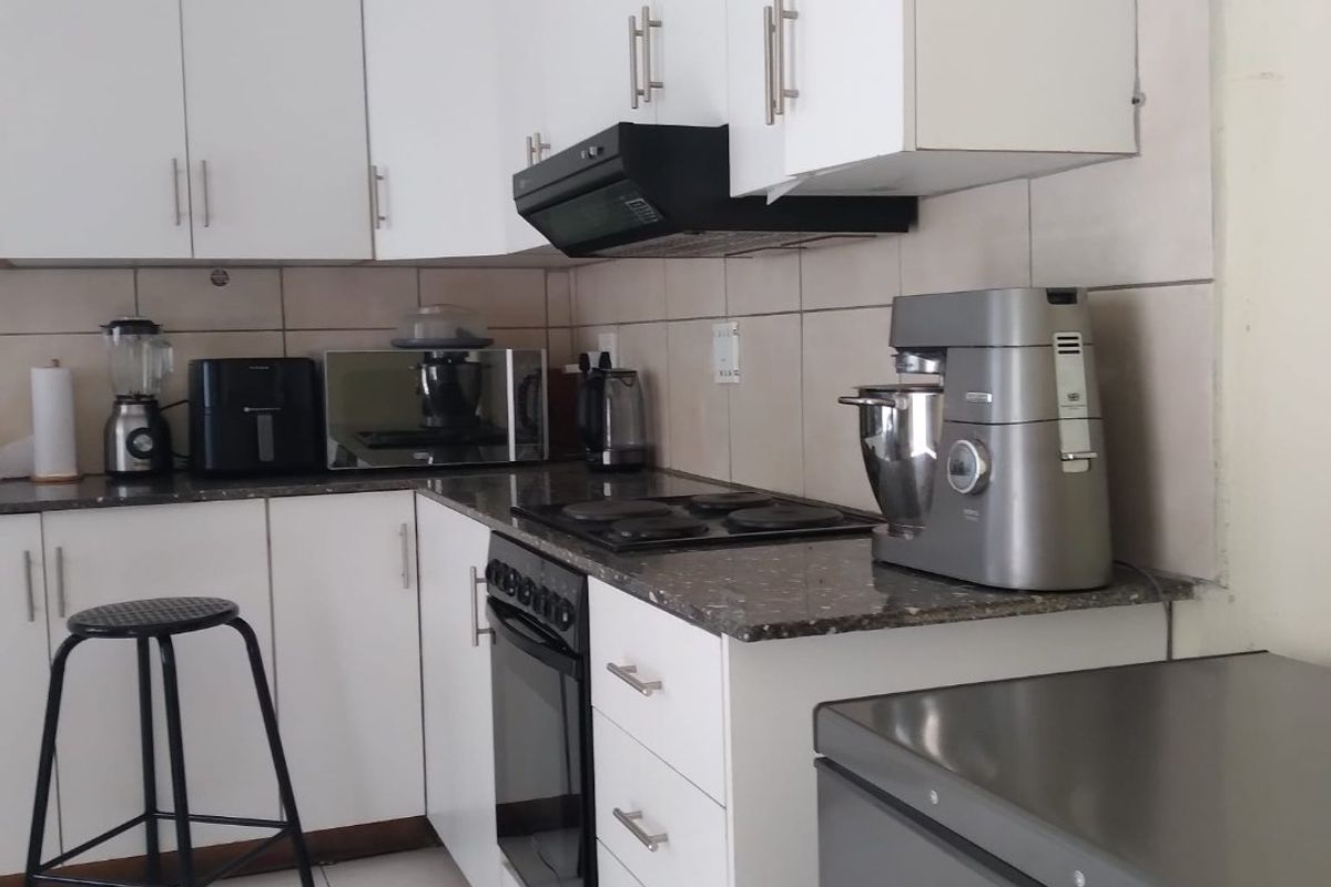 A functional kitchen featuring white cabinetry, granite countertops, a built-in oven with electric hob, and a tiled backsplash.
