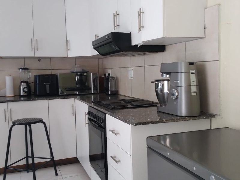 A functional kitchen featuring white cabinetry, granite countertops, a built-in oven with electric hob, and a tiled backsplash.
