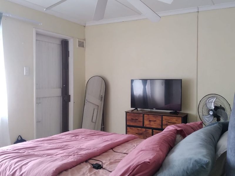 A functional bedroom featuring a ceiling fan, neutral wall finishes, and a classic timber door.