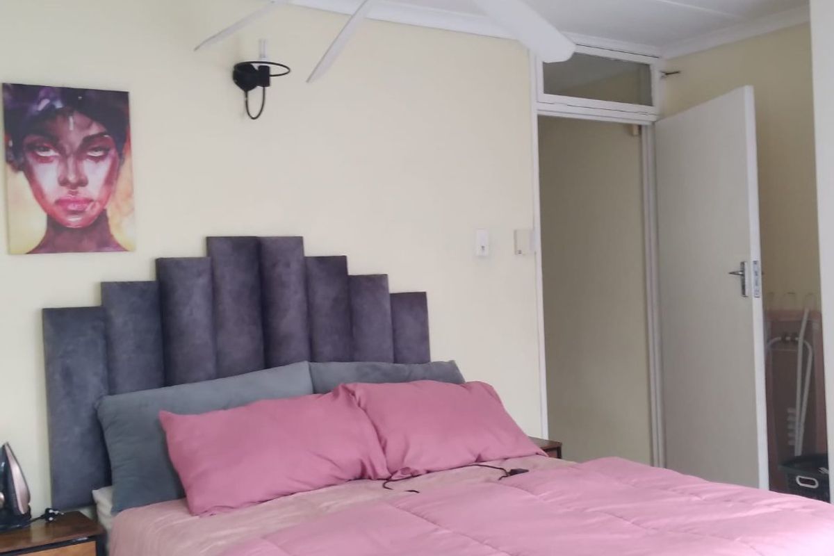 A bedroom featuring a ceiling fan, wall-mounted lighting, and a transom window above the doorway, providing a functional and well-lit sleeping space.
