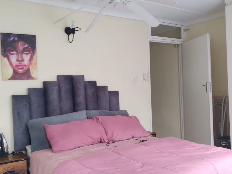 A bedroom featuring a ceiling fan, wall-mounted lighting, and a transom window above the doorway, providing a functional and well-lit sleeping space.