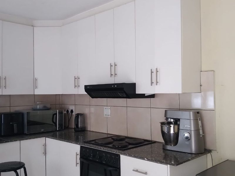 A functional kitchen featuring white cabinetry, granite countertops, a tiled backsplash, and integrated appliances including an oven, hob, and extractor fan.