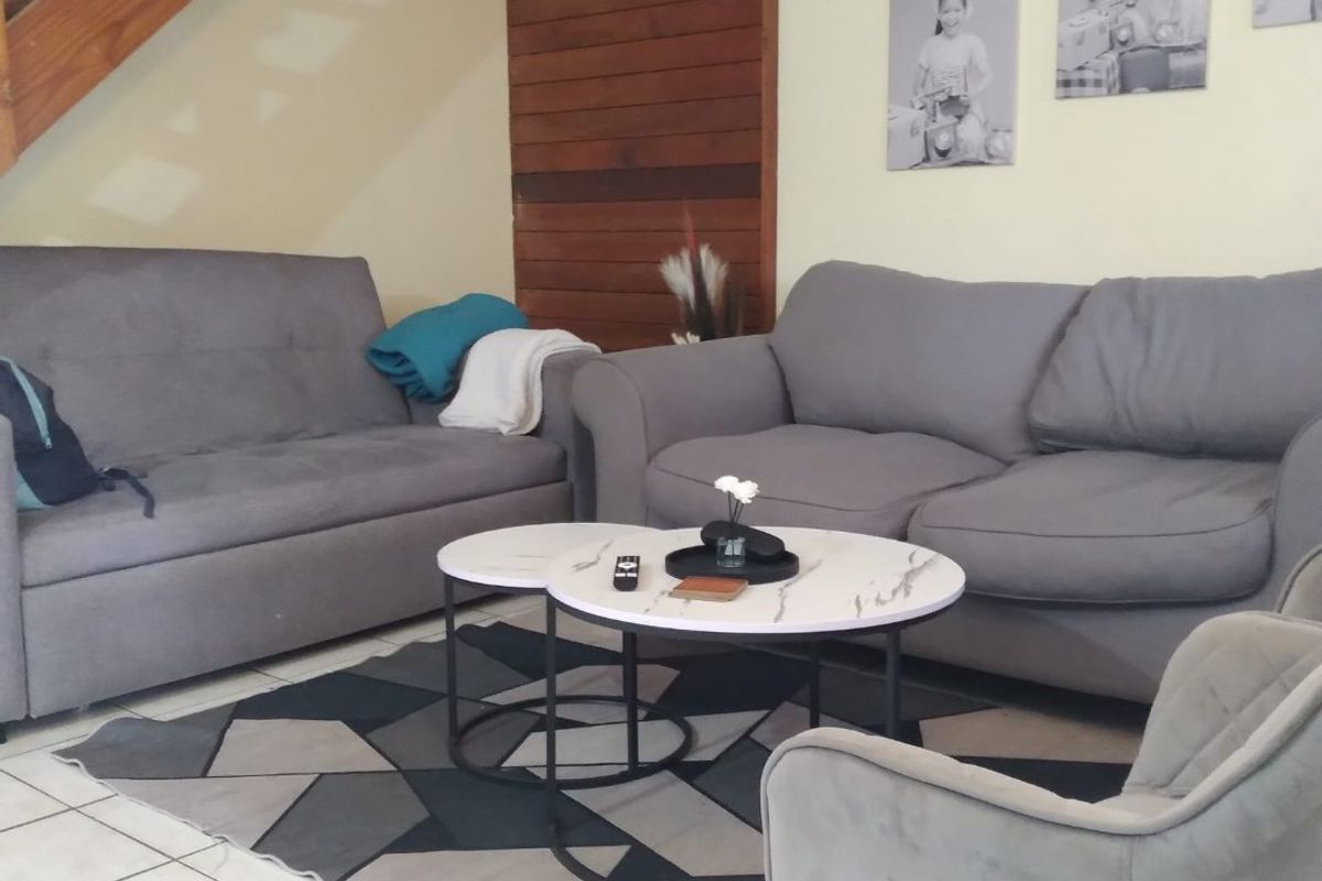 A living room area featuring ceramic floor tiles, timber wall paneling, and an open wooden staircase leading to the upper level.