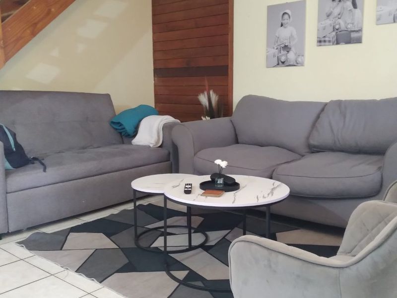 A living room area featuring ceramic floor tiles, timber wall paneling, and an open wooden staircase leading to the upper level.