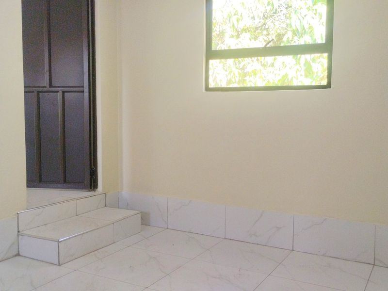 A clean, empty entry area featuring light-colored tiled flooring, a raised step, and a window providing natural light.