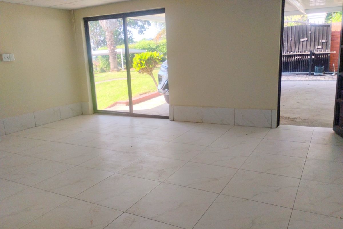 An empty, open-plan living area featuring light-colored floor tiles, recessed ceiling lighting, and a sliding glass door providing access to the garden.