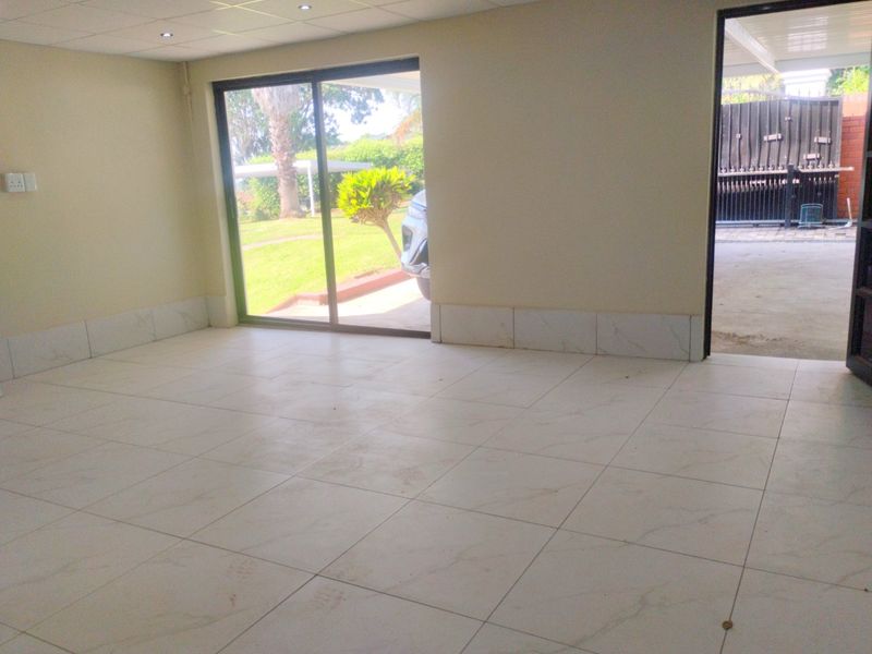 An empty, open-plan living area featuring light-colored floor tiles, recessed ceiling lighting, and a sliding glass door providing access to the garden.