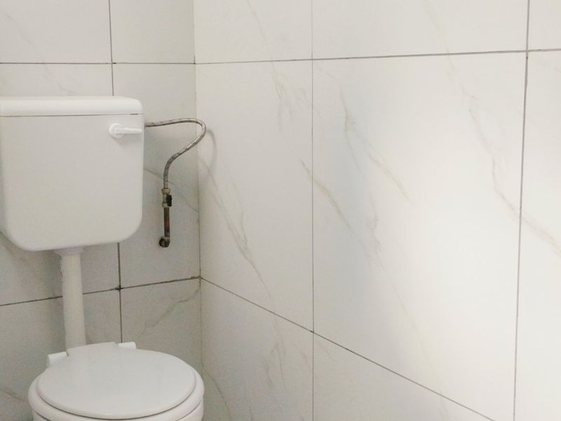 A compact bathroom featuring white marble-effect wall and floor tiles with a standard white toilet suite.