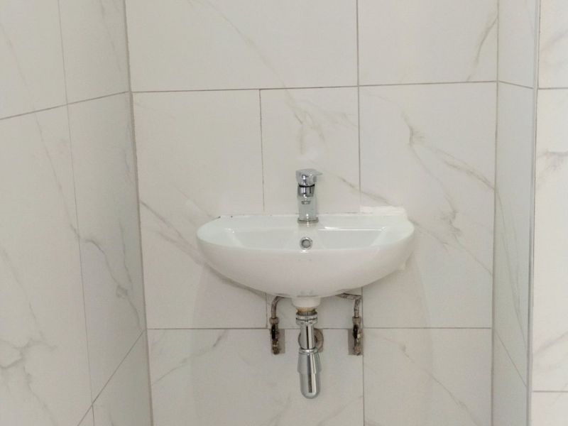 A minimalist bathroom featuring a wall-mounted basin with chrome fixtures, set against elegant marble-effect tiled walls and flooring.