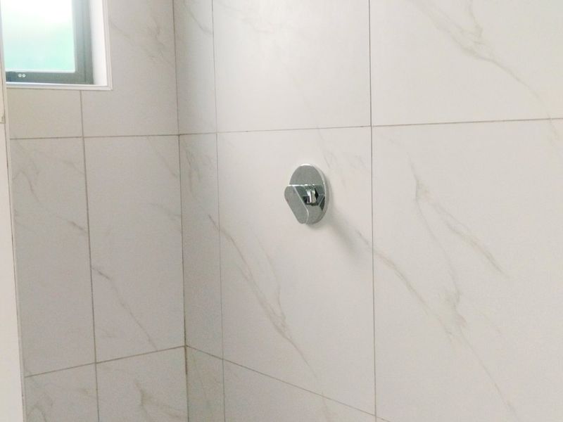 A modern shower enclosure featuring marble-look wall tiles, a rainfall shower head, and a mosaic-tiled floor.