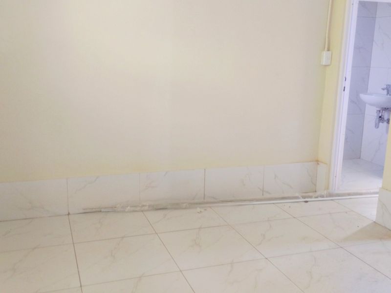 An empty bedroom featuring tiled flooring and skirting, with an adjacent bathroom visible through the doorway. The space requires finishing touches.