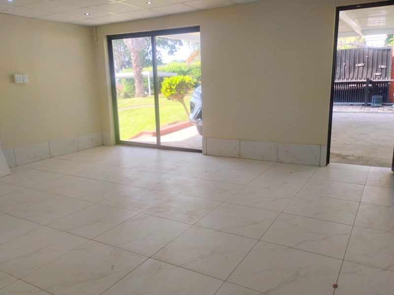 An empty, open-plan living area featuring light-colored floor tiles, recessed ceiling lighting, and a sliding glass door providing access to the garden.