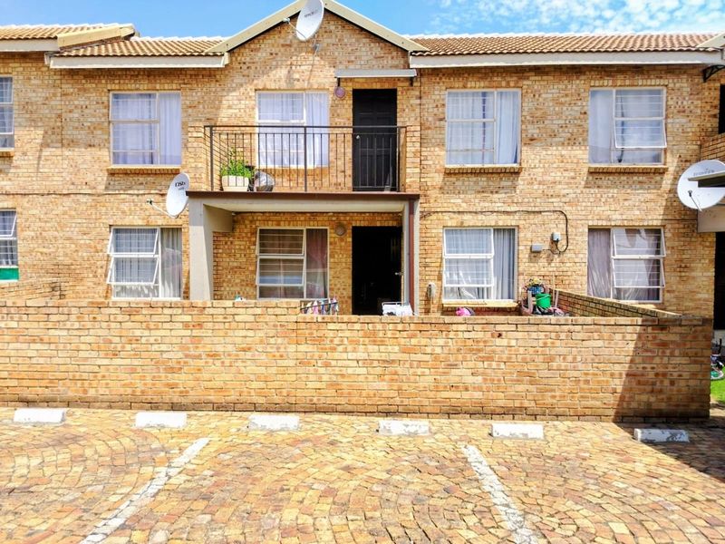 Front elevation of a face brick townhouse complex featuring a paved driveway, private balcony with iron railing, and secure window fittings.