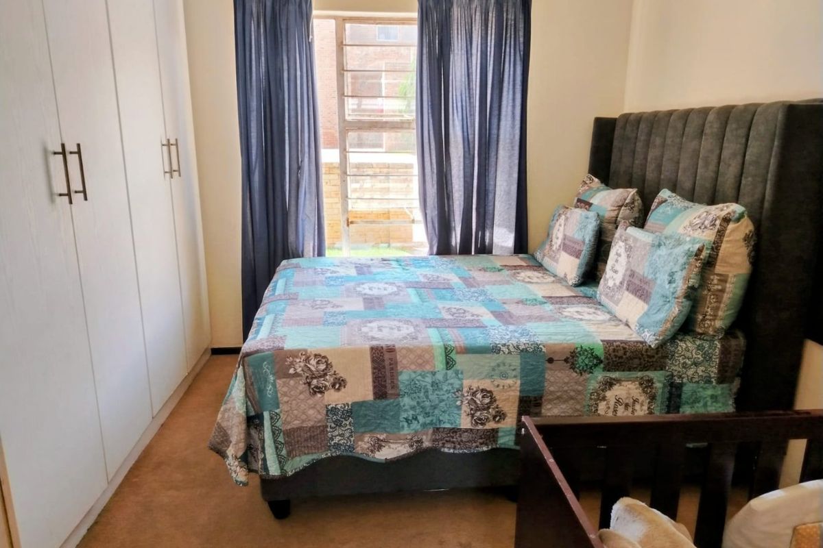 A functional bedroom featuring built-in cupboards, carpeted flooring, and a louvered window providing natural light.